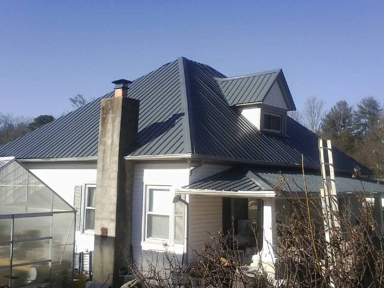 Dark blue standing seam metal roof on a white farmhouse with dormer — Slate & Tile Roof Repair by Roofing Brothers in Nederland