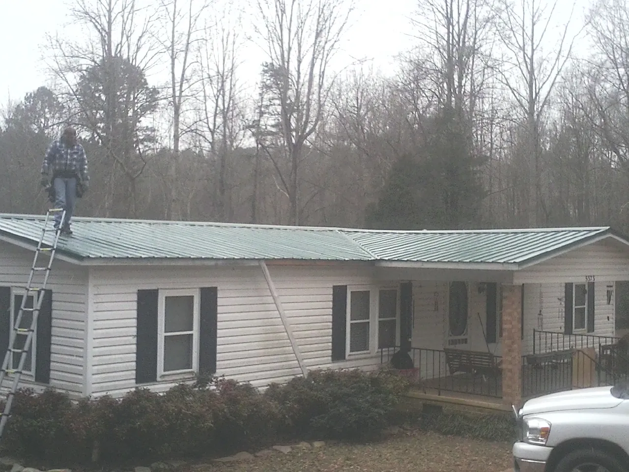 Worker on a ladder beside a new green metal roof on a ranch home in Nederland