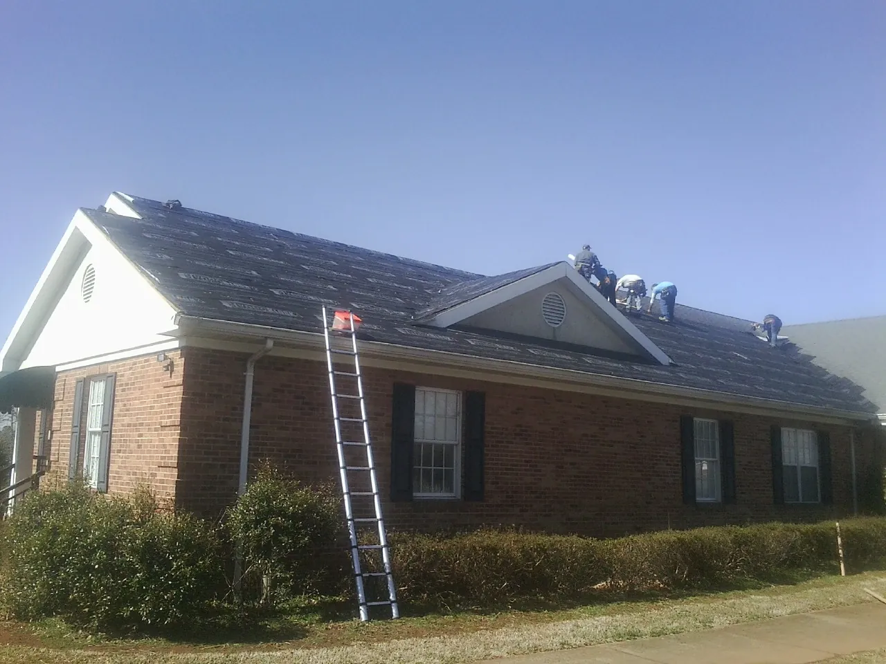 Crew tearing shingles off a brick ranch roof with a ladder set — Metal Roof Repair work by our crew in Nederland