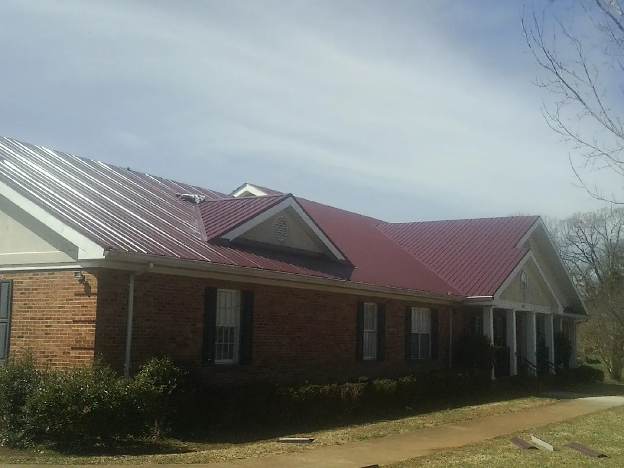 Red metal roof with gabled entries on a long brick building, from a Hail Damage Roof Repair job in Nederland
