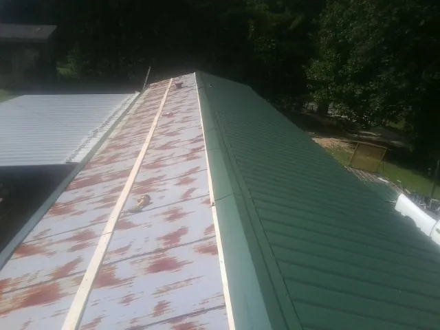 Old rusted panels beside newly installed green metal roofing — Wind Damage Roof Repair by Roofing Brothers in Nederland