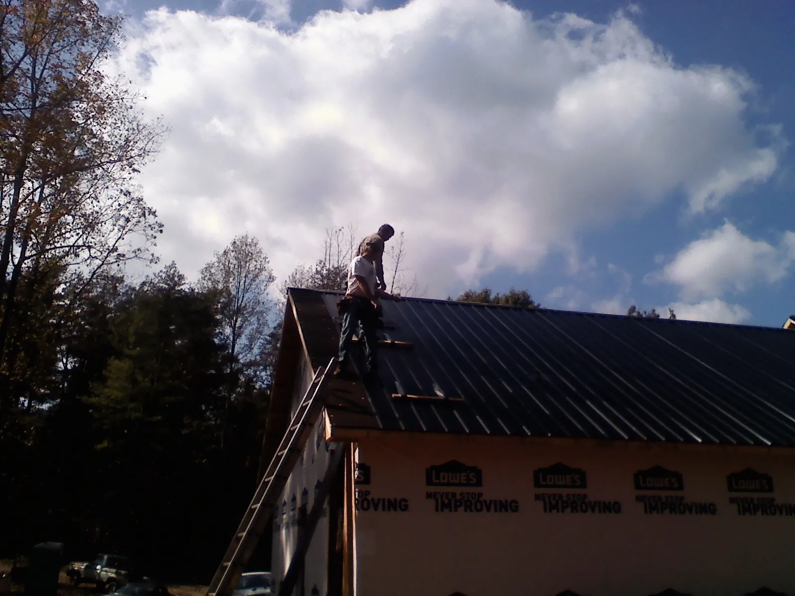 Roofer fastening dark metal panels high against a cloudy sky, from a Roof Inspection job in Nederland