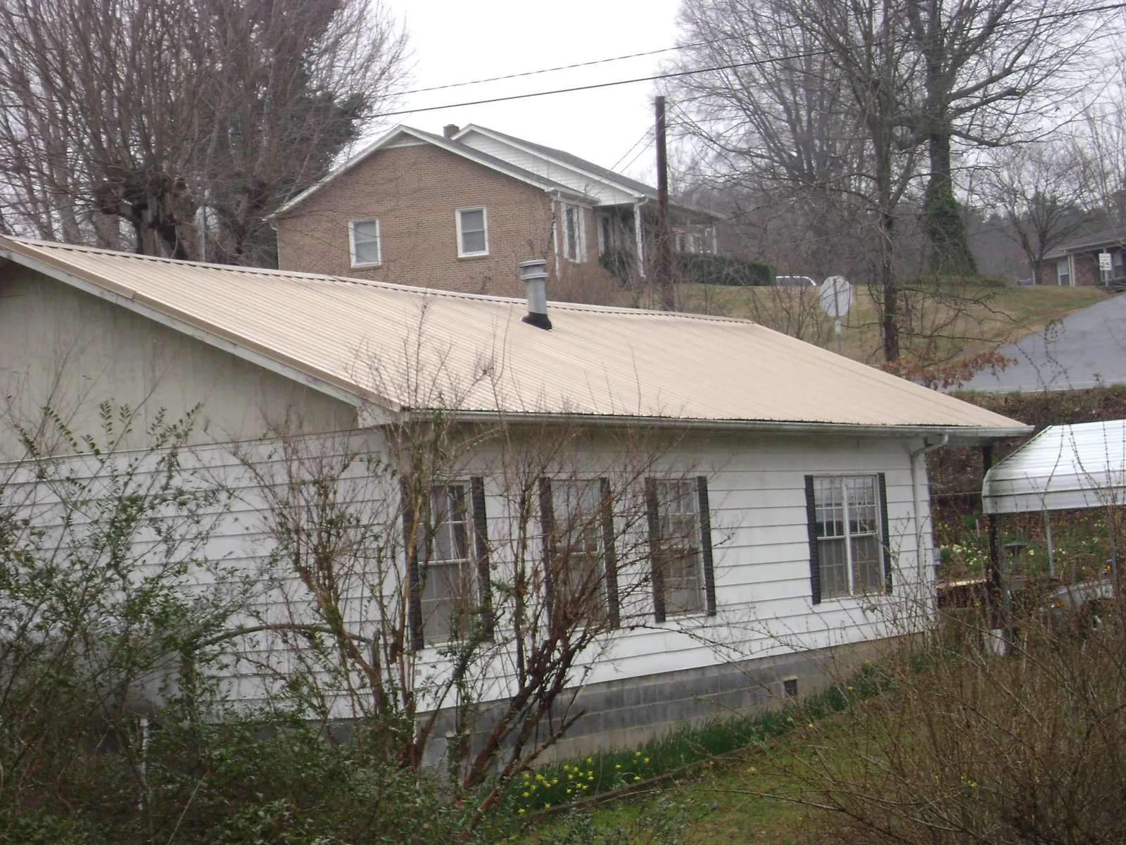 Tan metal roof on a white sided house set into a hillside — Commercial Roofing by Roofing Brothers in Nederland