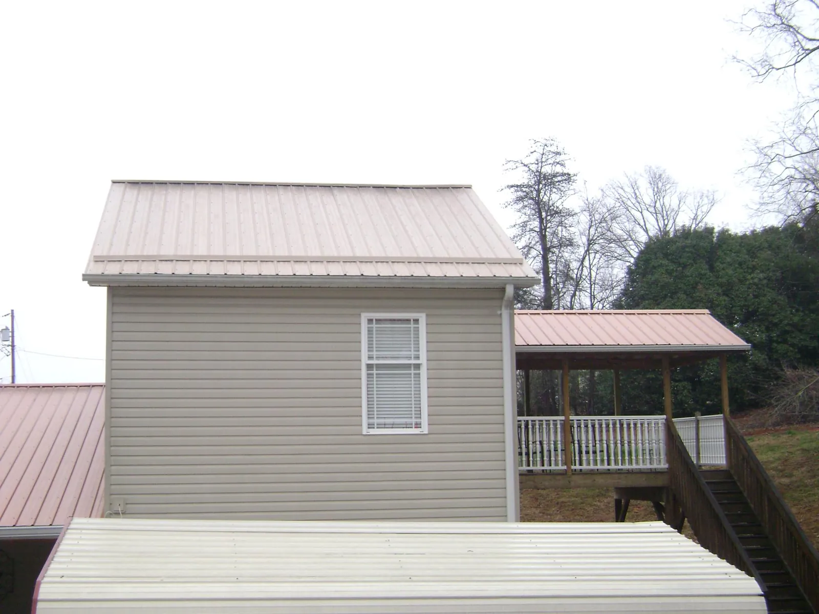 Tan metal roofs on a two story addition and attached porch, from a Roof Replacement job in Nederland